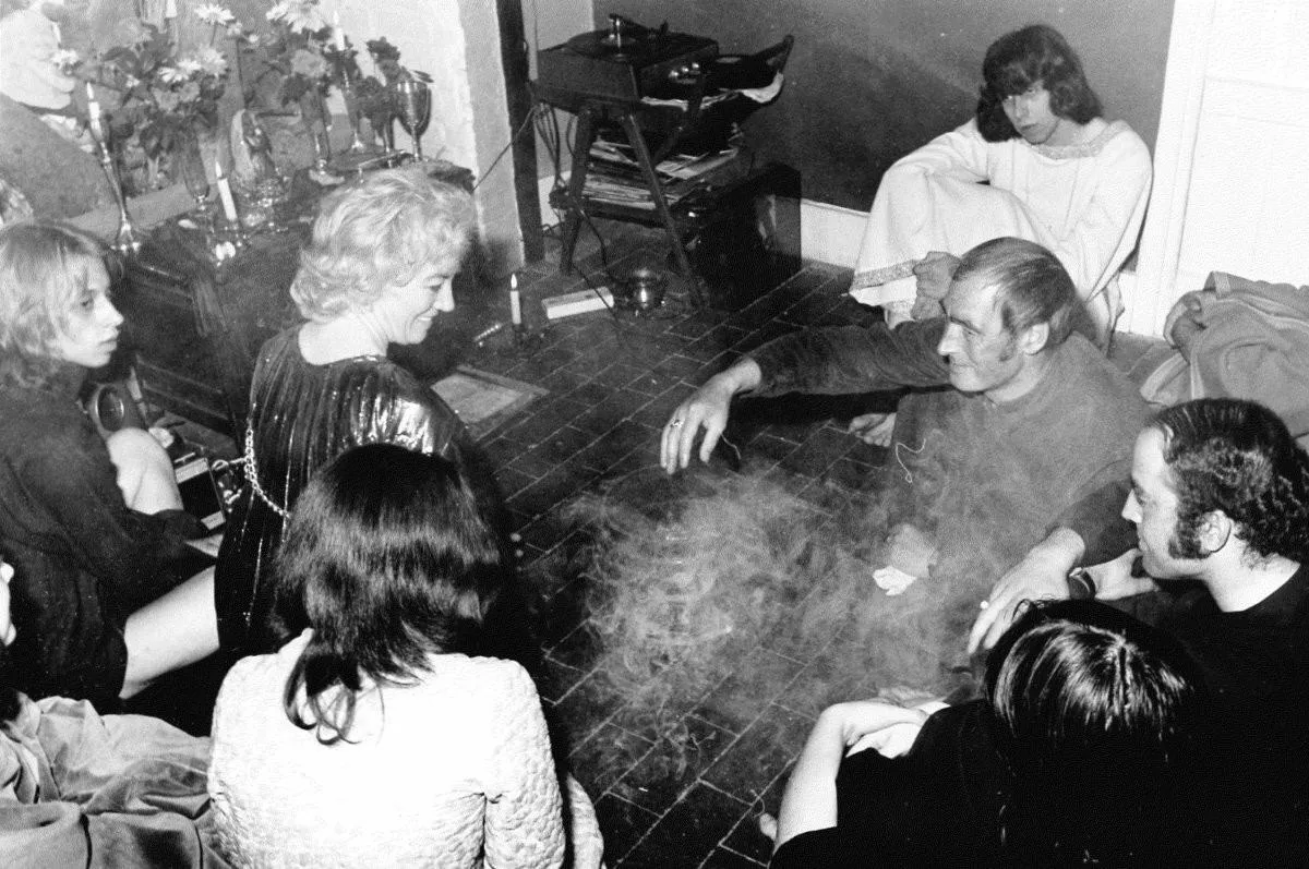 Alex and Maxine Sanders gathered with coven members in a candlelit room, incense smoke rising between them.