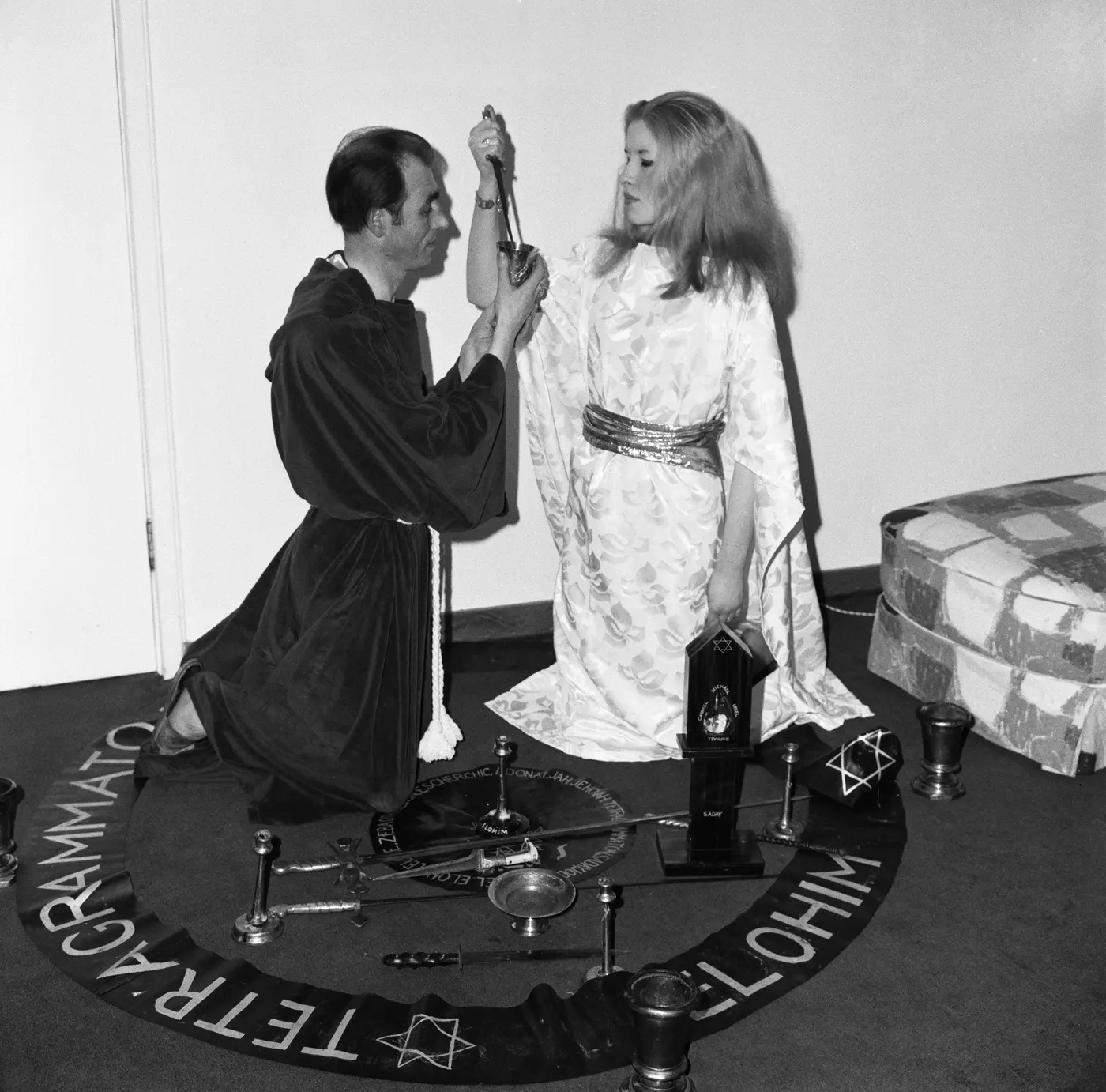 Two robed figures working within a ritual circle inscribed with divine names, surrounded by the working tools.