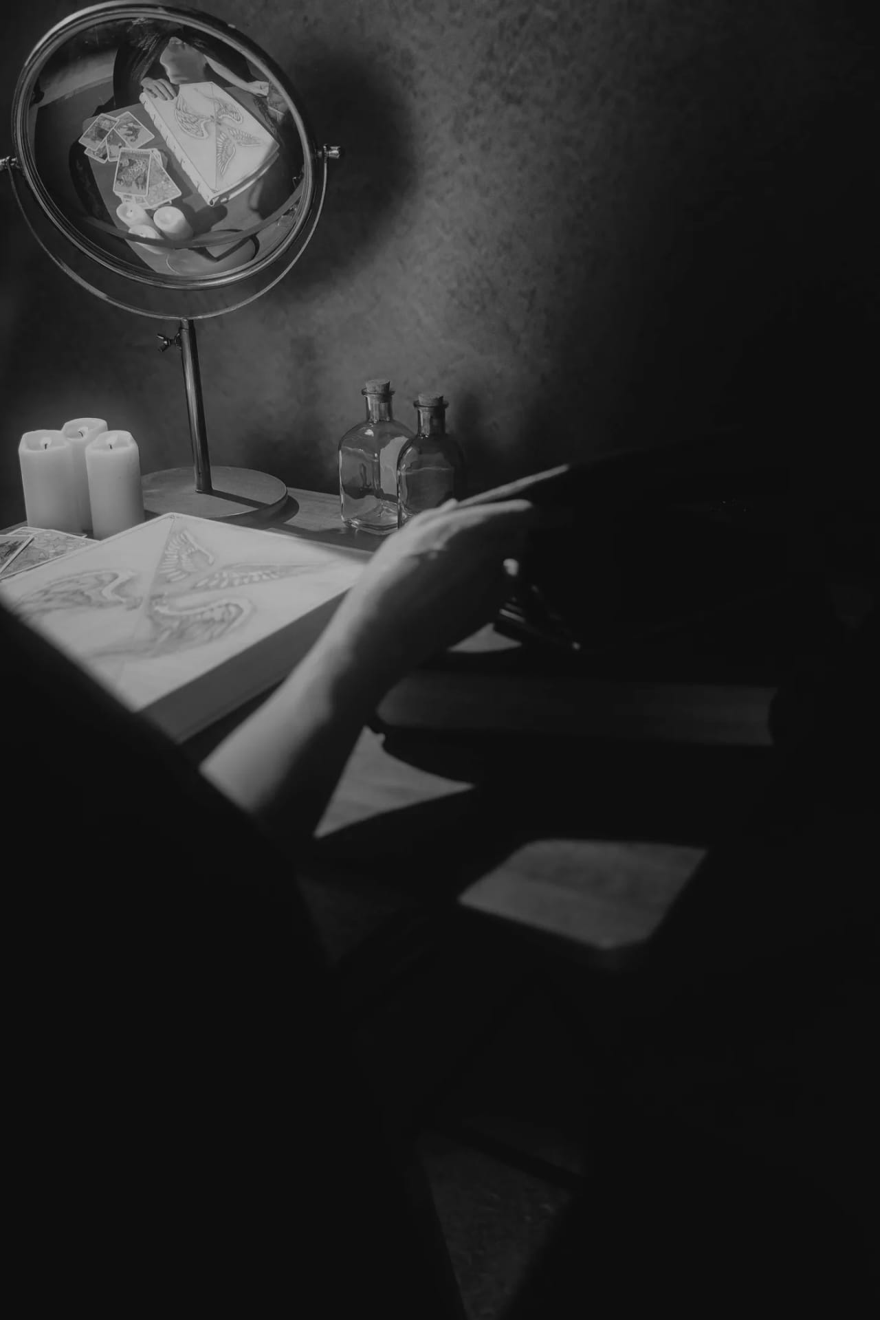 Sharon Day at a desk by candlelight, reading, with a round mirror and a bound book before her.
